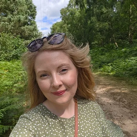 Tanya Rejek smiling, with sunglasses pushed up on her head, on a woodland path lined with ferns